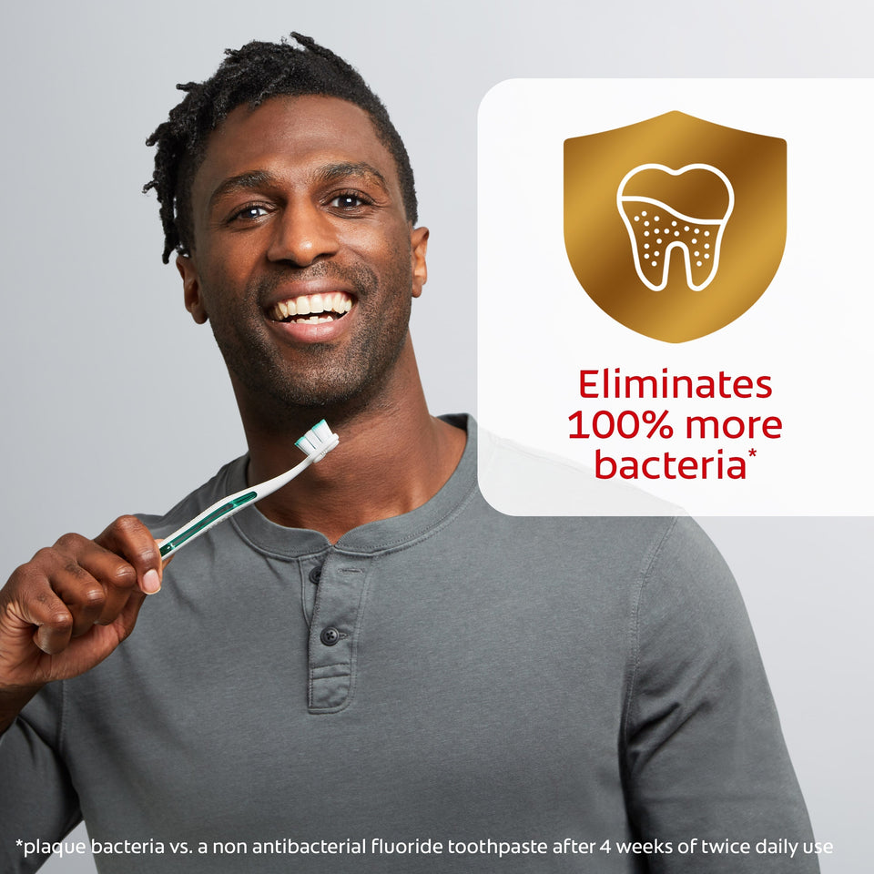 A man smiling while holding a toothbrush. In text: Eliminates 100% more bacteria*. *Plaque bacteria vs. a non-antibacterial fluoride toothpaste after 4 weeks of twice daily use. 