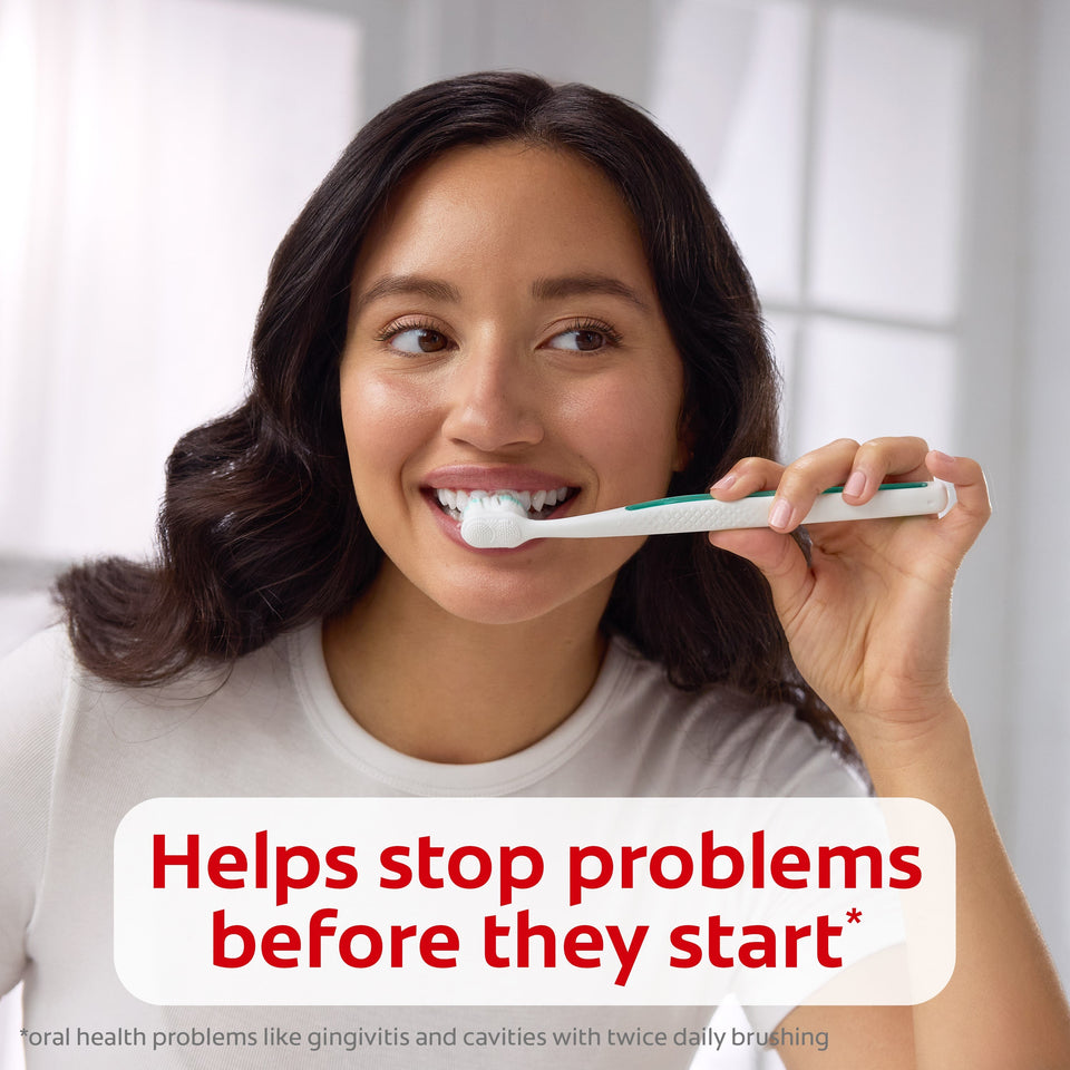 A woman smiling while brushing her teeth with Colgate Total Active Prevention Gum Protect Whitening Toothpaste. In text: Helps stop problems before they start*. *Oral health problems like gingivitis and cavities with twice daily brushing. 