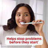 A woman smiling while brushing her teeth with Colgate Total Active Prevention Gum Protect Whitening Toothpaste. In text: Helps stop problems before they start*. *Oral health problems like gingivitis and cavities with twice daily brushing. 