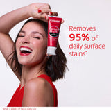 A woman smiling while holding a tube of Colgate Optic White with Charcoal Teeth Whitening Toothpaste. In text: Removed 95% of daily surface stains*. After 2 weeks of twice daily use. 