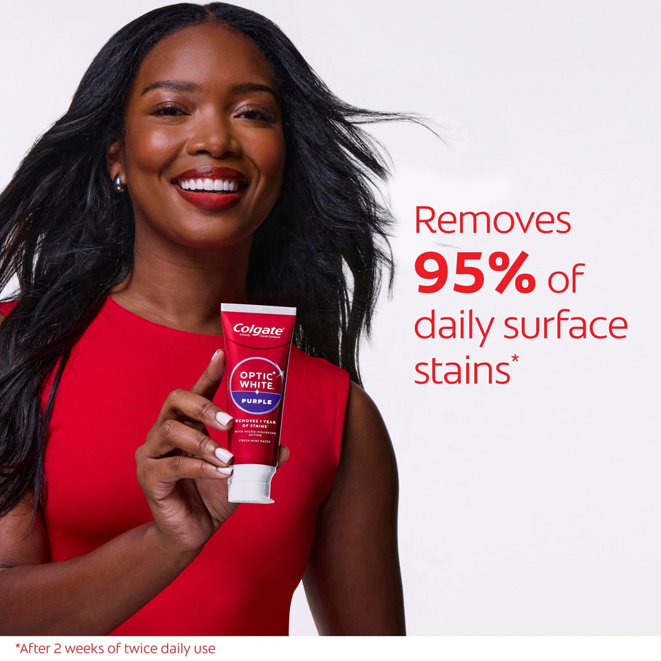 A woman with white teeth smiling and holding a tube of Colgate Optic White Purple Toothpaste for Teeth Whitening. In text: Removes 95% of daily surface stains*. *After 2 weeks of twice daily use. 