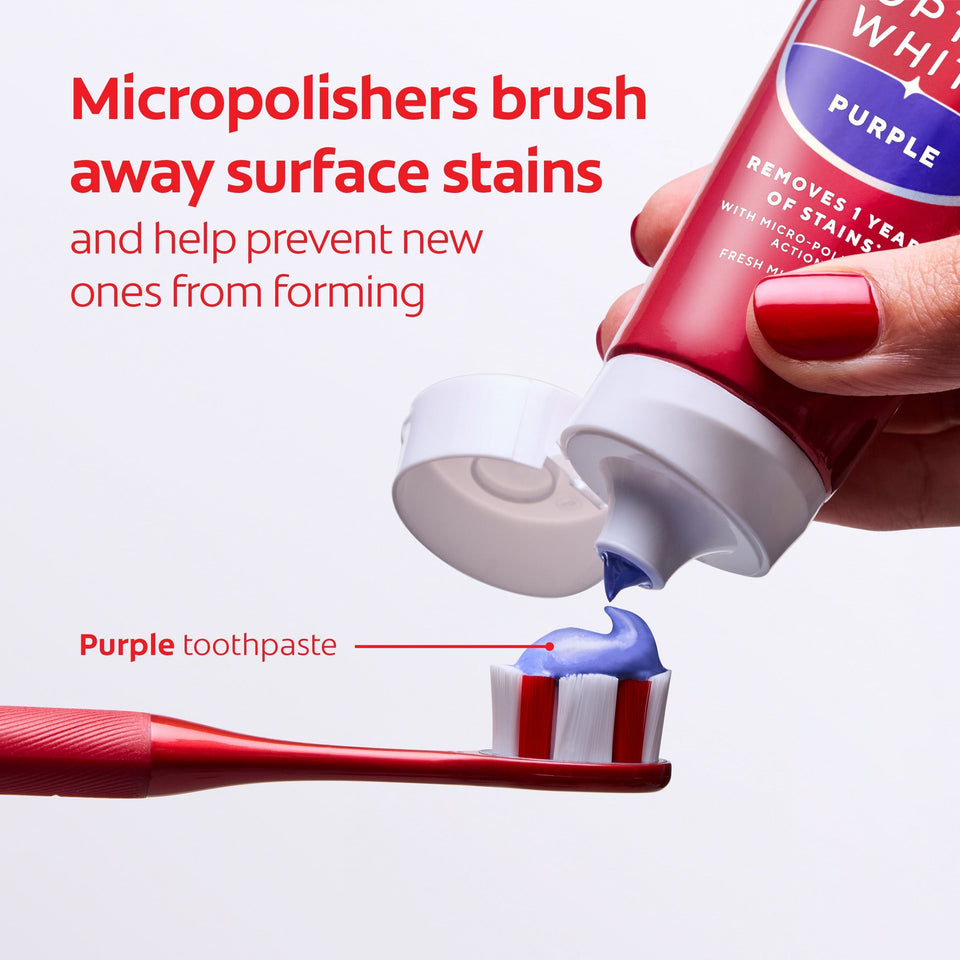 Colgate Optic White Purple Toothpaste for Teeth Whitening being squeezed onto a toothbrush. In text: Micropolishers brush away surface stains and help prevent new ones from forming. Purple toothpaste. 
