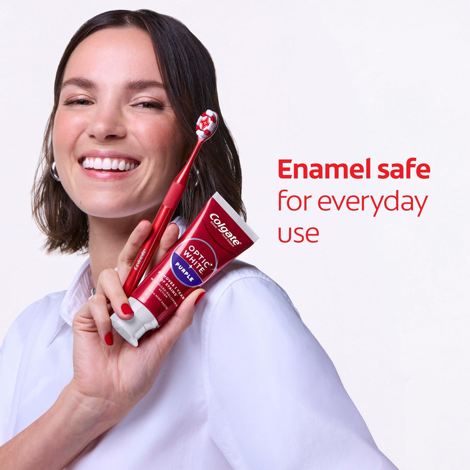 A woman with white teeth smiling while she holds a red Colgate toothbrush and a tube of Colgate Optic White Purple Toothpaste for Teeth Whitening. In text: Enamel safe for everyday use. 